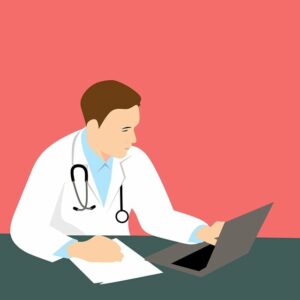 Movement Disorder Specialist - Phot of a doctore sitting at thr computer with papers on desk for discussion on Benefits of seeing an MDS
